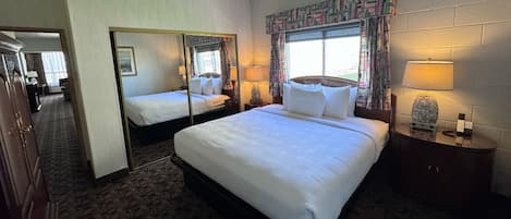 Quarto de hotel com uma cama grande, um espelho, mesa de cabeceira com abajur e janela com cortinas.