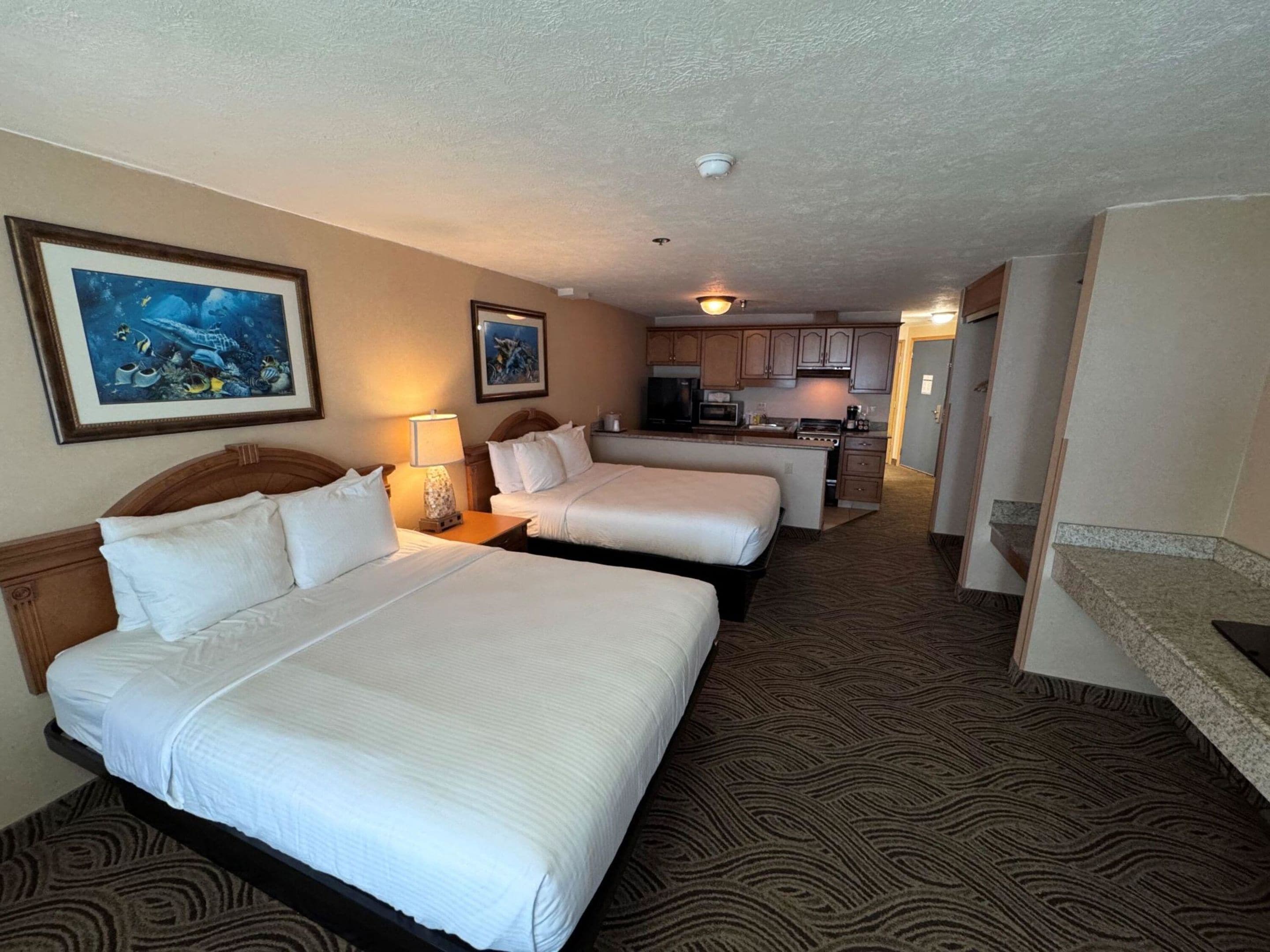A hotel room with two beds, a kitchenette, and a bathroom.