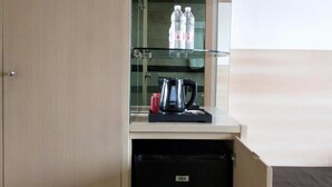 A compact room with a kitchenette area featuring a GEA refrigerator, a GEA coffee maker, and a glass cabinet with water bottles. - Asyana Kemayoran Jakarta (Jakarta)