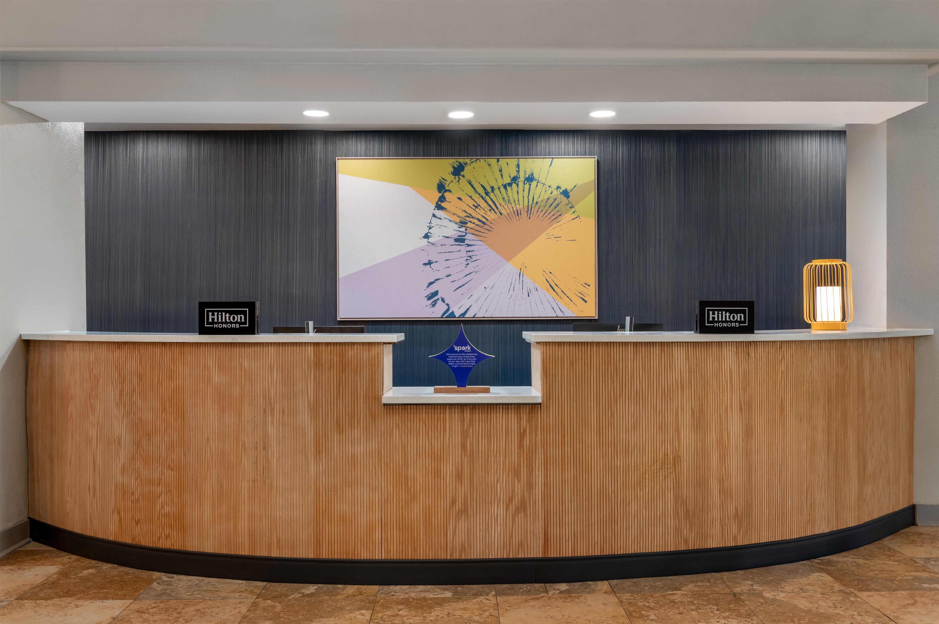 A reception desk with a modern design, featuring a wooden finish and a large abstract painting above it.