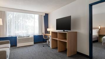 Een hotelkamer met een bed, een bureau met een televisie, een stoel, een raam met gordijnen en een luchtverfrisser aan de muur.