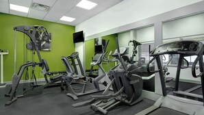 A gym with various exercise machines, a television, and a green wall. - Spark by Hilton Watertown (Watertown)