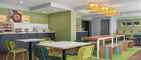 Una cocina moderna con una isla central, sillas verdes y una lámpara colgante amarilla.