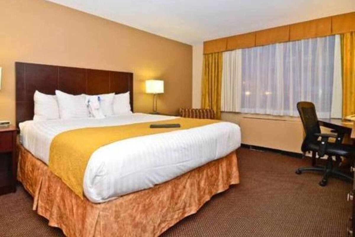 Una habitación de hotel con una cama grande, un escritorio, una silla, una lámpara y una ventana con cortinas.