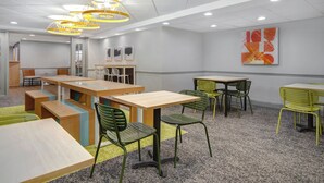 A modern interior with tables and chairs, a ceiling with recessed lighting, and a wall with abstract art. - Spark by Hilton Watertown (Watertown)
