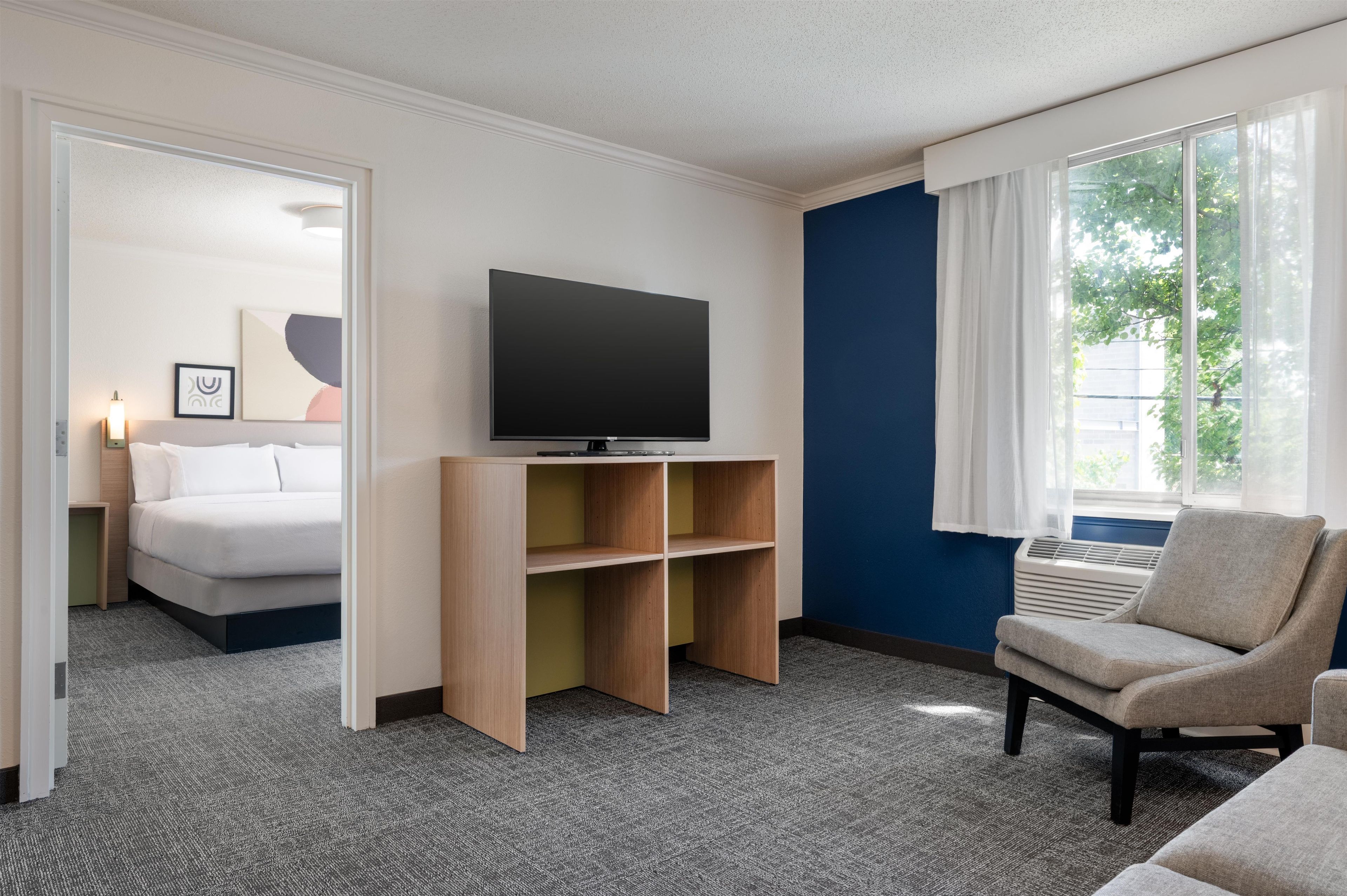 A hotel room with a bed, a television on a stand, a chair, and a window with curtains.