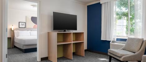 A hotel room with a bed, a television on a stand, a chair, and a window with curtains.