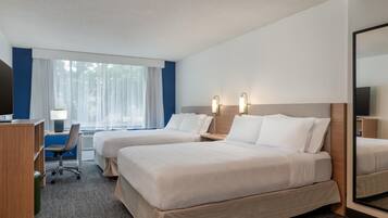 A hotel room with two beds, a desk, a chair, a TV, and a large mirror.