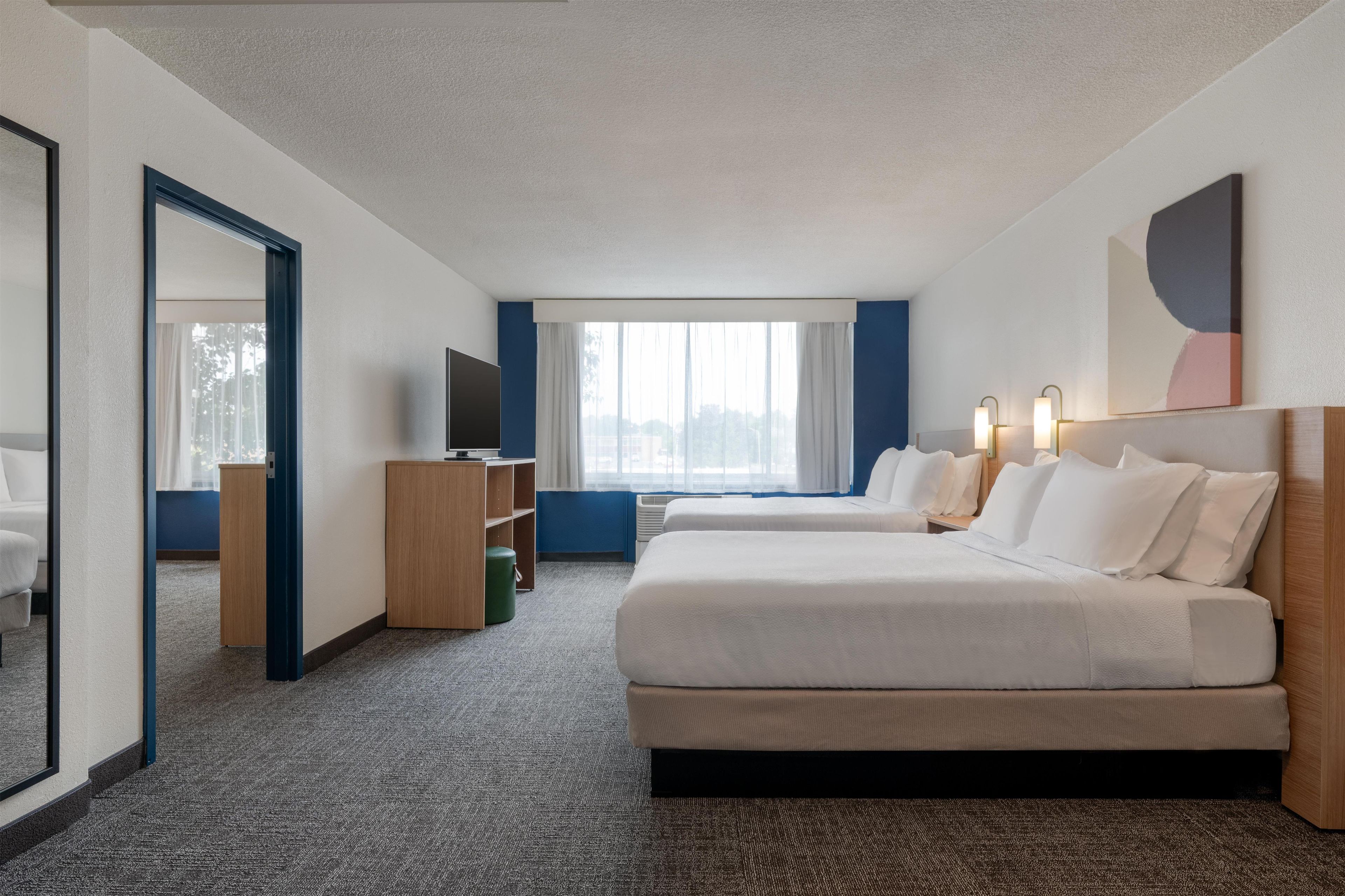 A hotel room with a large bed, a TV, a desk, and a window with curtains.