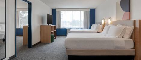 A hotel room with a large bed, a TV, a desk, and a window with curtains.