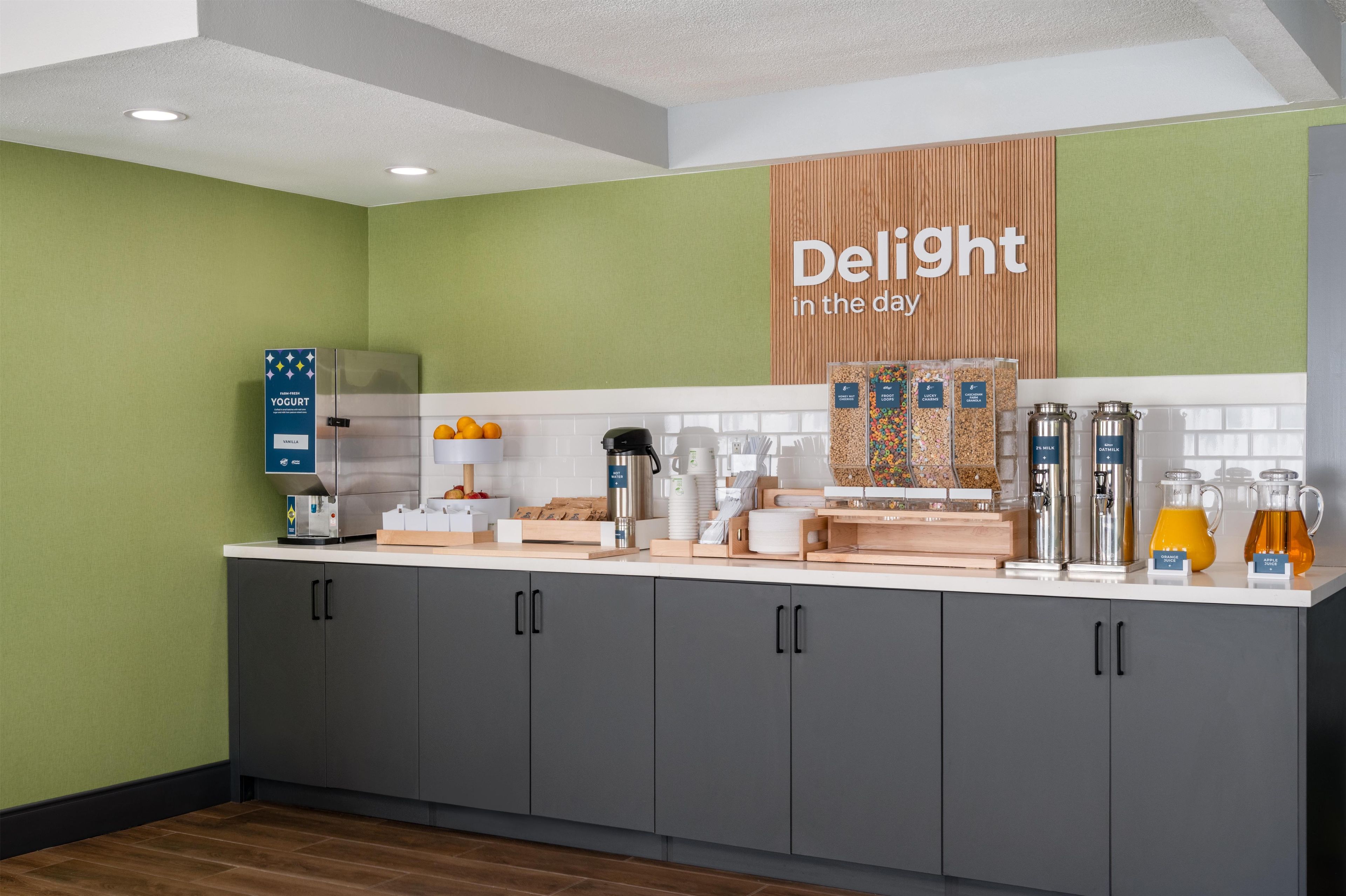 A modern kitchen area with a breakfast bar, a yogurt dispenser, and a variety of breakfast items.