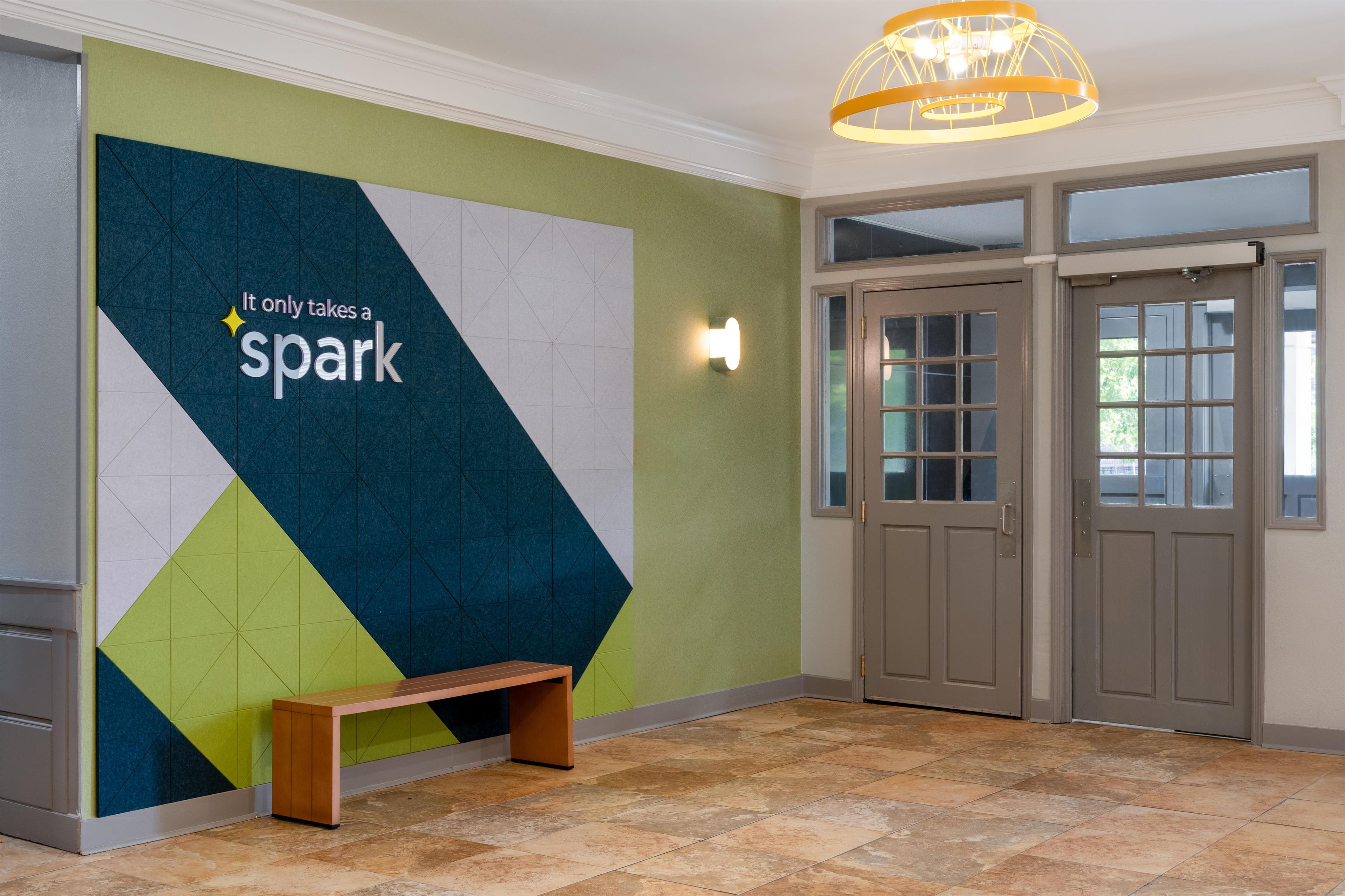 A lobby with a geometric wall design, a bench, and double doors.