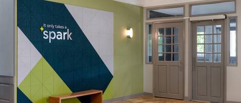 A lobby with a geometric wall design, a bench, and double doors.