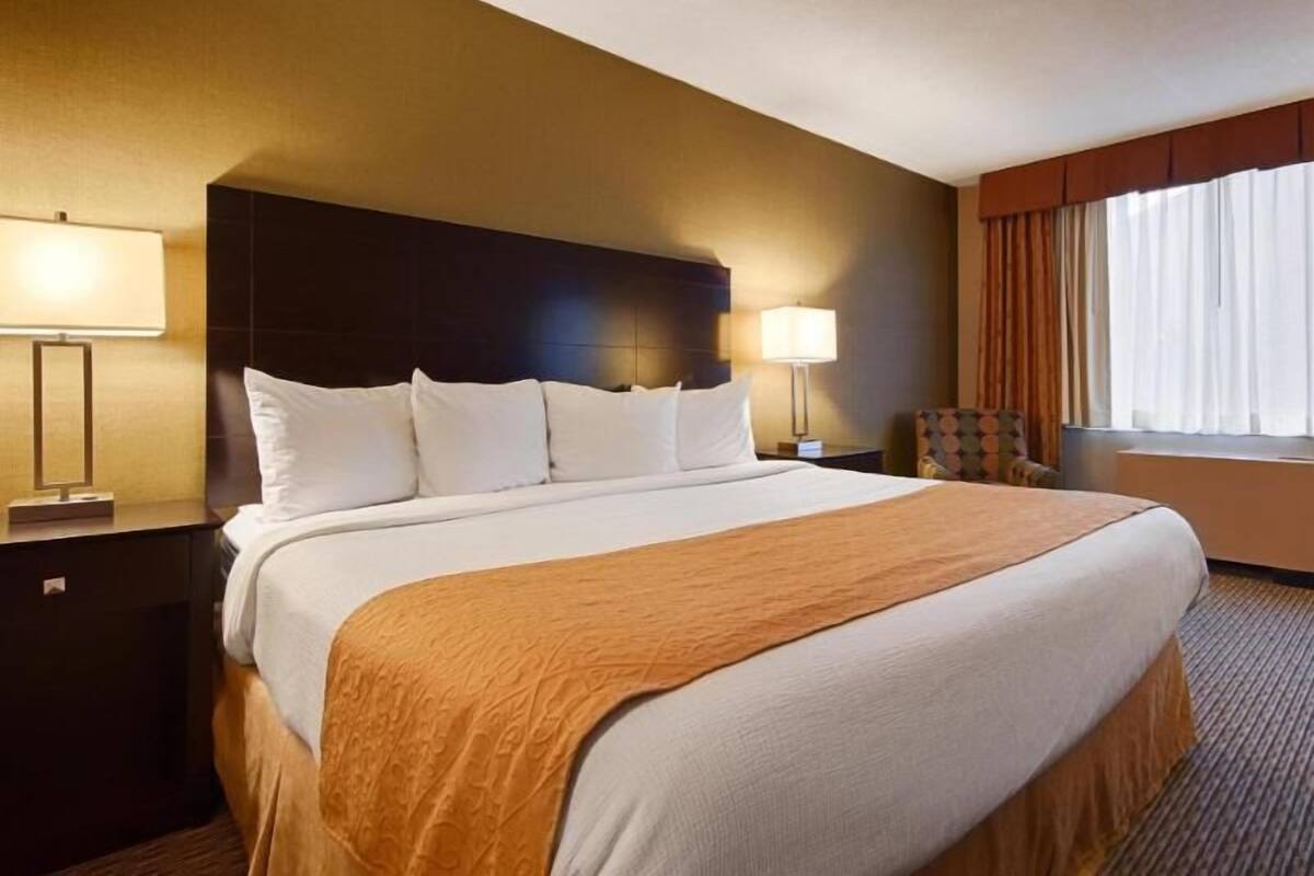 Habitación de hotel con una cama grande, dos lámparas de noche, una silla y una ventana con cortinas.
