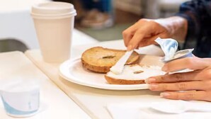 Jemand bestreicht eine Scheibe Brot mit Butter auf einem Teller.