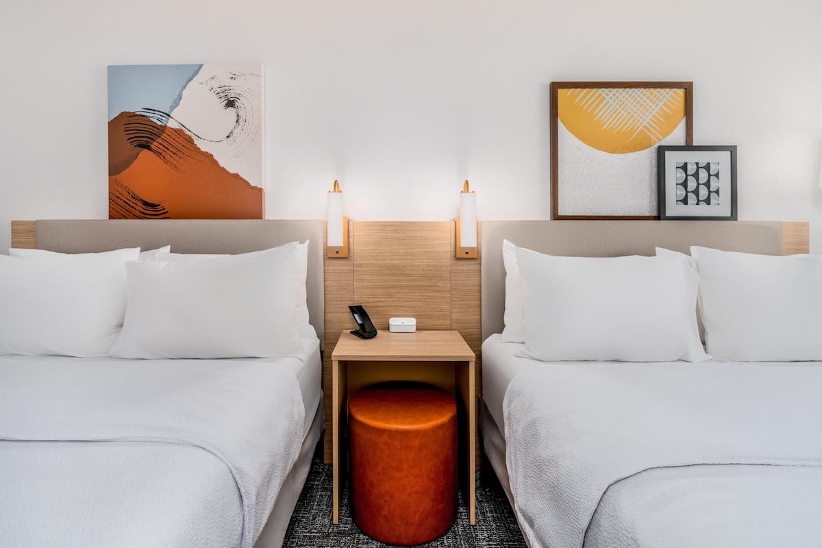 Ein Hotelzimmer mit zwei Betten, einem Nachttisch mit Telefon und Lampe sowie Bildern an den Wänden.