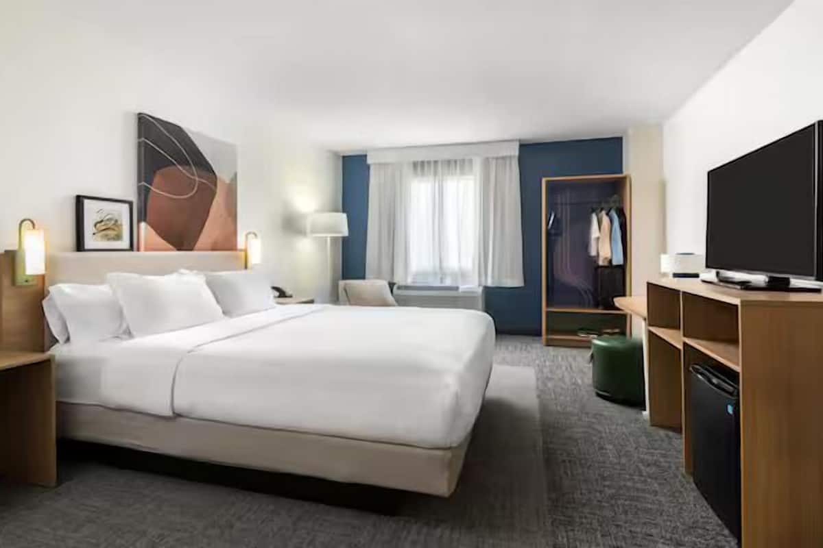 Ein Hotelzimmer mit einem großen Bett, Nachttischen, einem Fernseher, einem Kleiderschrank und einem Fenster mit Vorhängen.