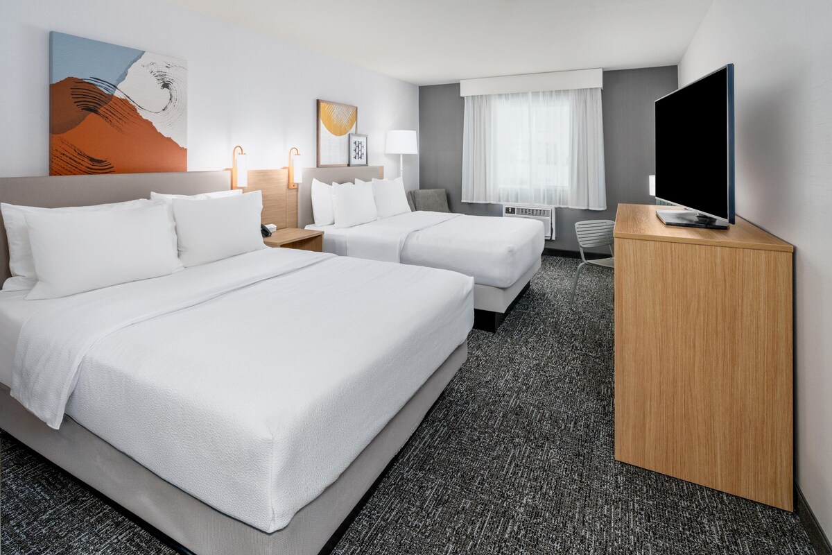 Ein Hotelzimmer mit zwei Betten, einem Schreibtisch, einem Fernseher und einem Bild an der Wand.