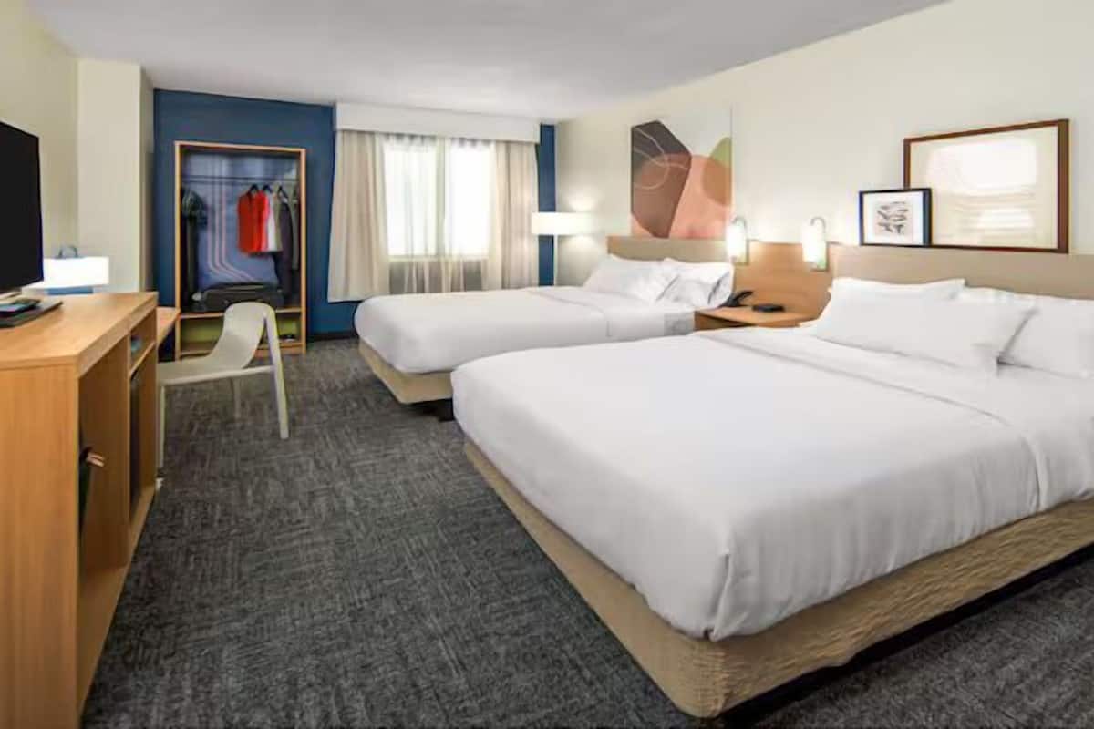 Ein Hotelzimmer mit zwei Betten, einem Schreibtisch, einem Stuhl, einem Kleiderschrank und einem Fernseher.