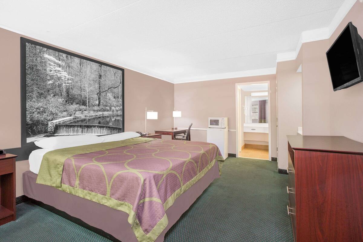A hotel room with a large bed, a desk, a chair, a television, and a bathroom visible through an open door.