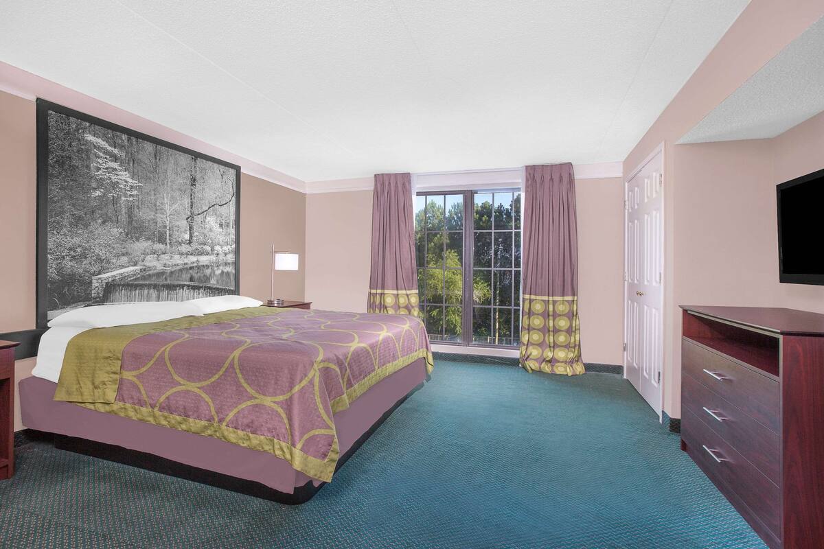 A hotel room with a large bed, a dresser, a television, and a window with curtains.