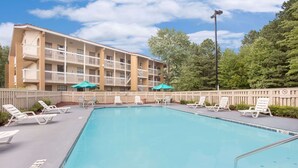 A swimming pool with lounge chairs and umbrellas, surrounded by a building with multiple balconies. - Super 8 by Wyndham Austell/Six Flags (Austell)