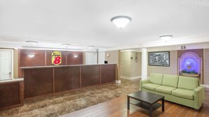 A lobby with a reception desk, a green sofa, and a tiled floor. - Super 8 by Wyndham Austell/Six Flags (Austell)