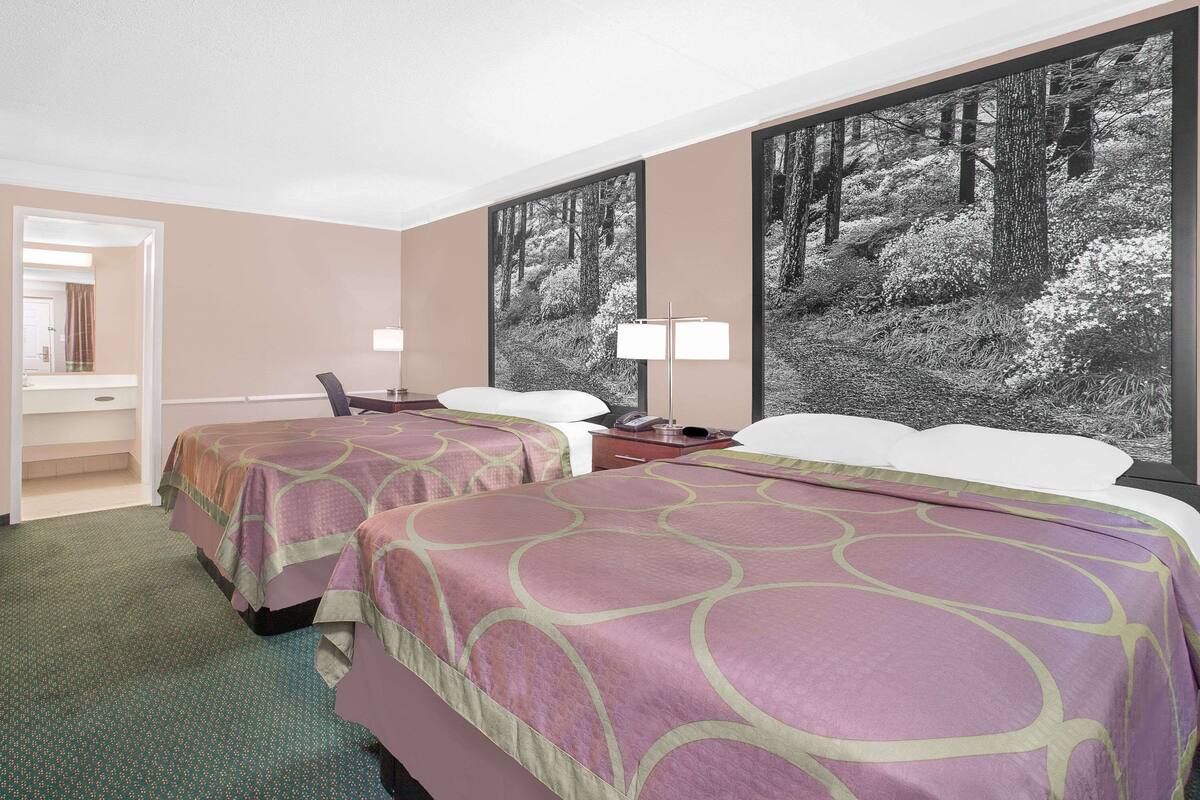 A hotel room with two beds, a desk, and a large window with a forest view.