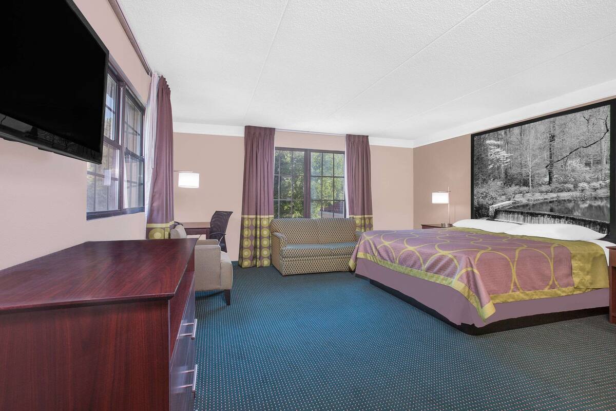 A hotel room with a bed, a desk, a sofa, and a window with curtains.
