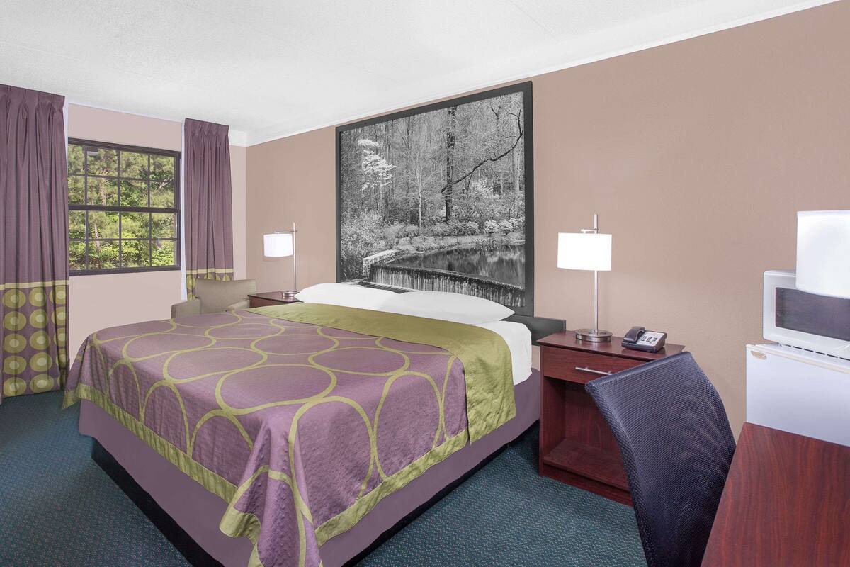 A hotel room with a large bed, a desk, a chair, a television, and a window with curtains.