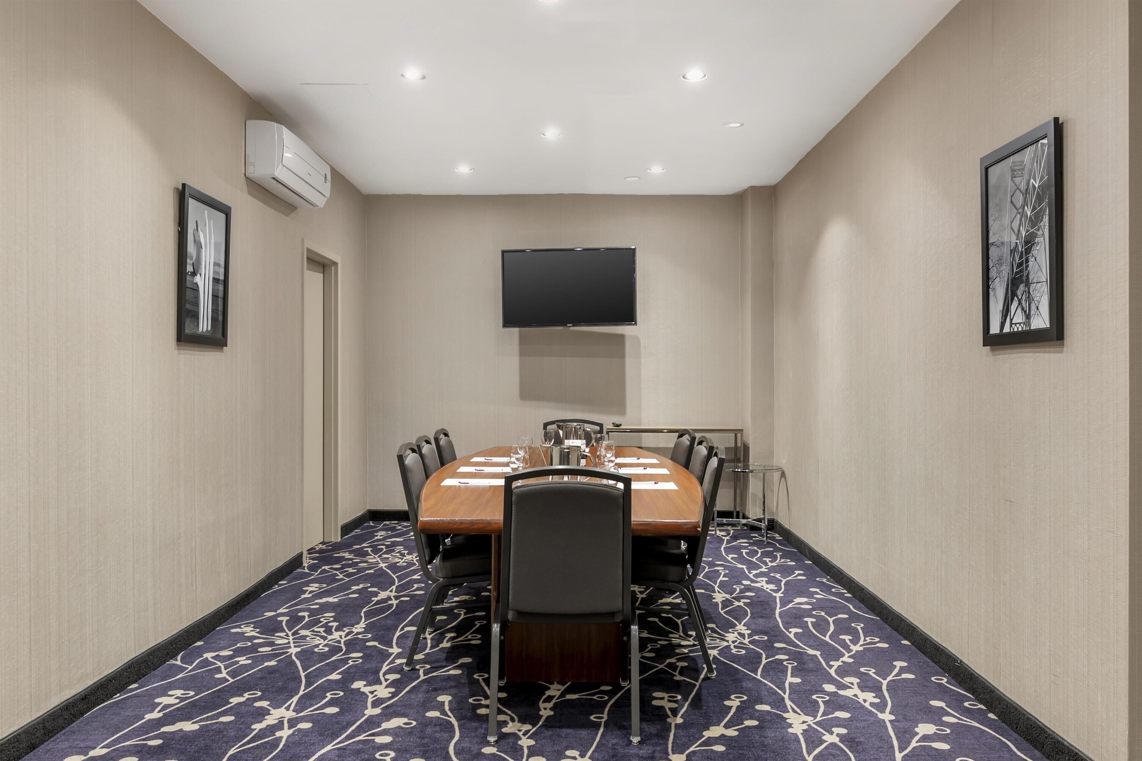 A conference room with a long table, chairs, a flat-screen TV, and framed artwork on the walls.