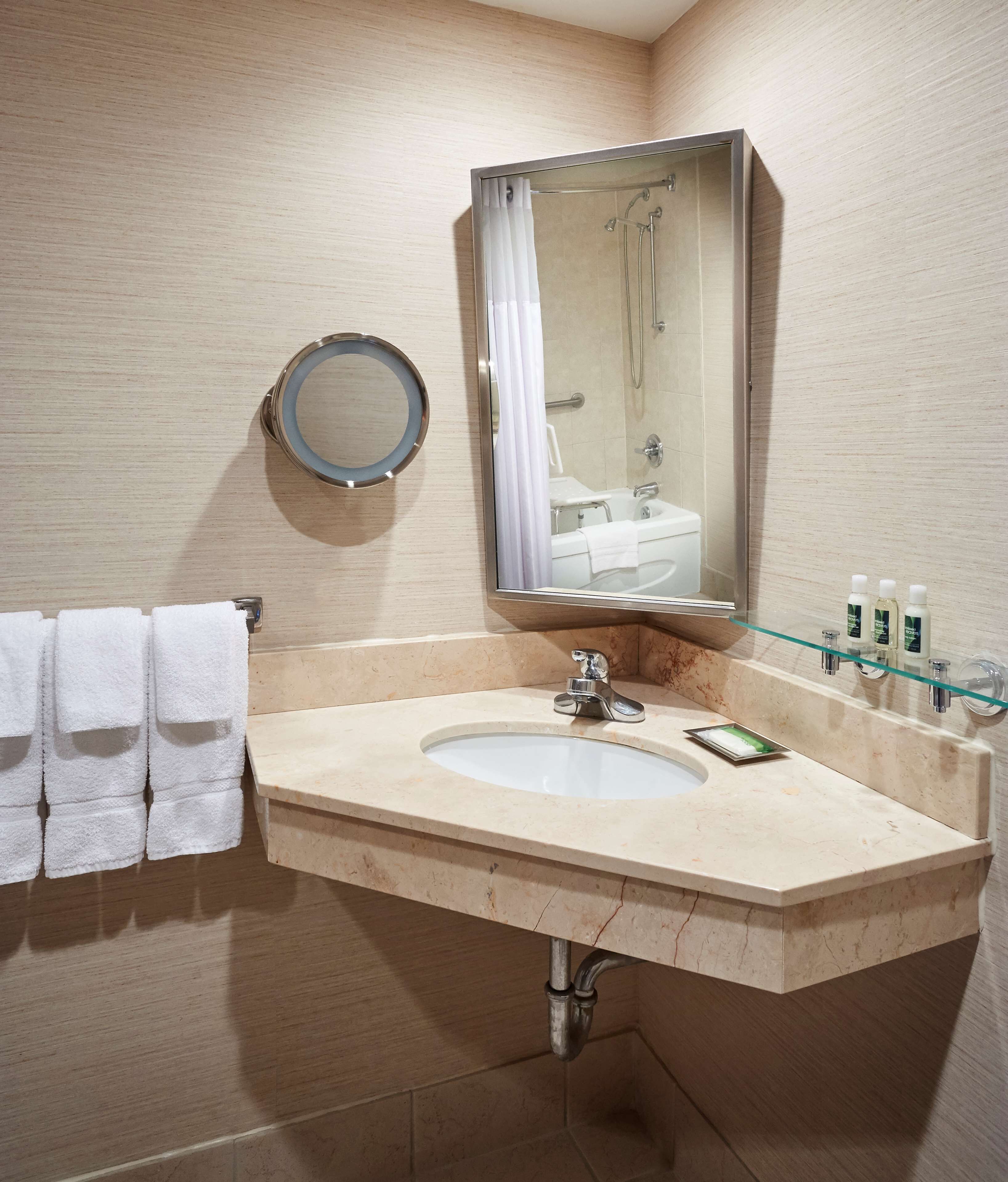 Un baño con lavamanos, espejo, toallero y artículos de aseo.