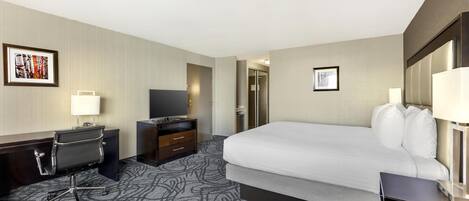 Una habitación de hotel con una cama grande, un escritorio con silla, un televisor y un armario.