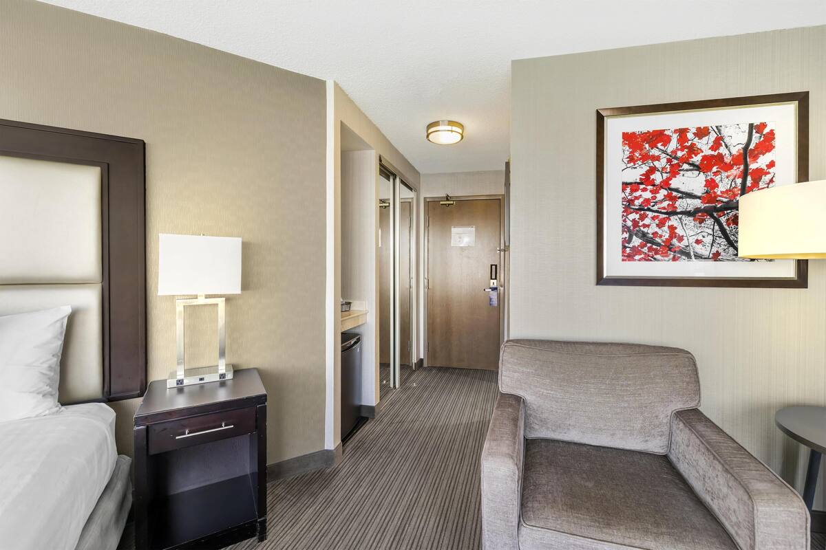 Habitación de hotel con cama, mesita de noche con lámpara, sofá e imagen enmarcadas en la pared.