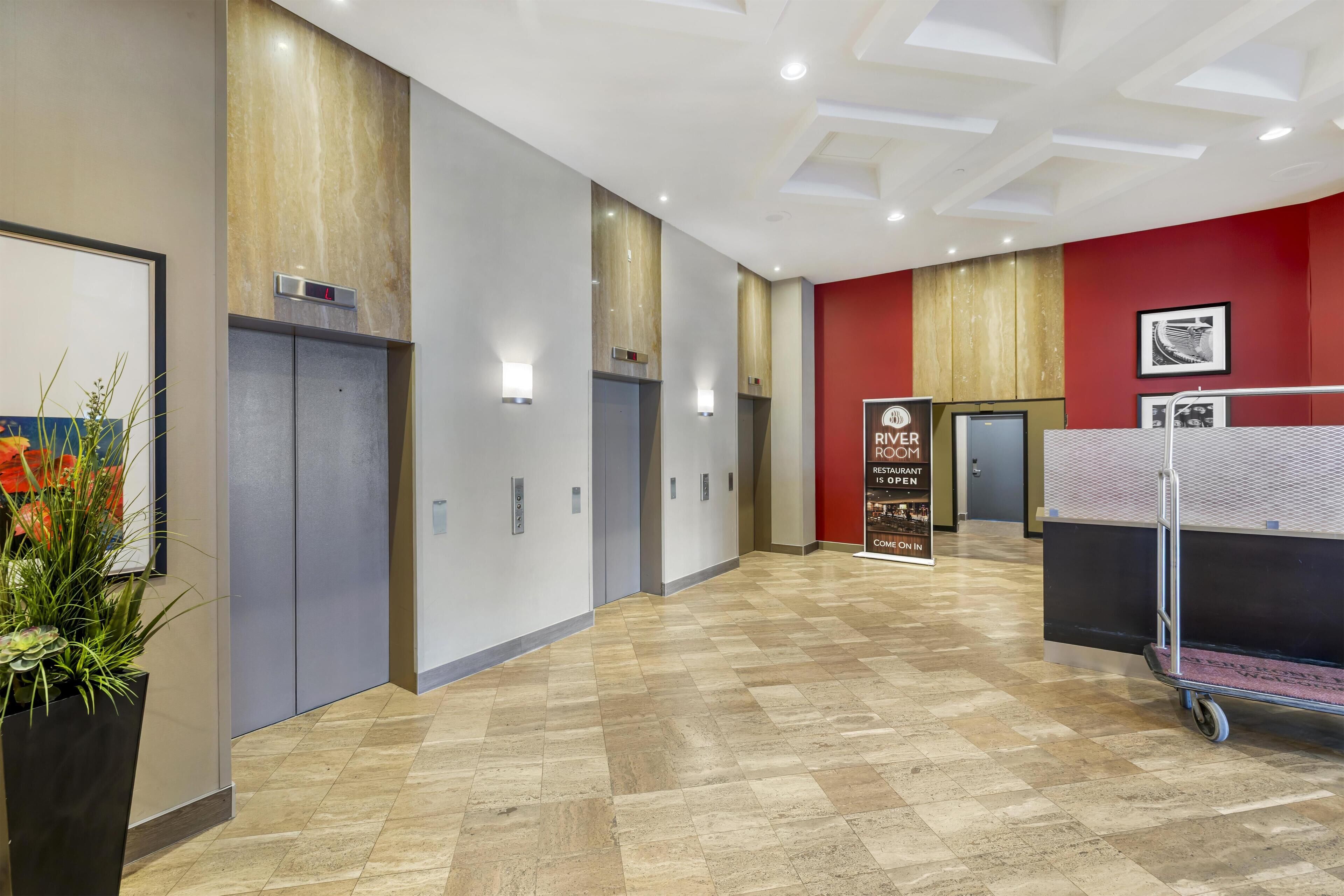 A hotel corridor with elevators, a reception desk, and a sign for a restaurant.