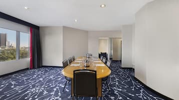 A conference room with a long table, chairs, and a city view through large windows.