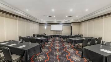 A conference room with tables, chairs, a projector screen, and a patterned carpet.