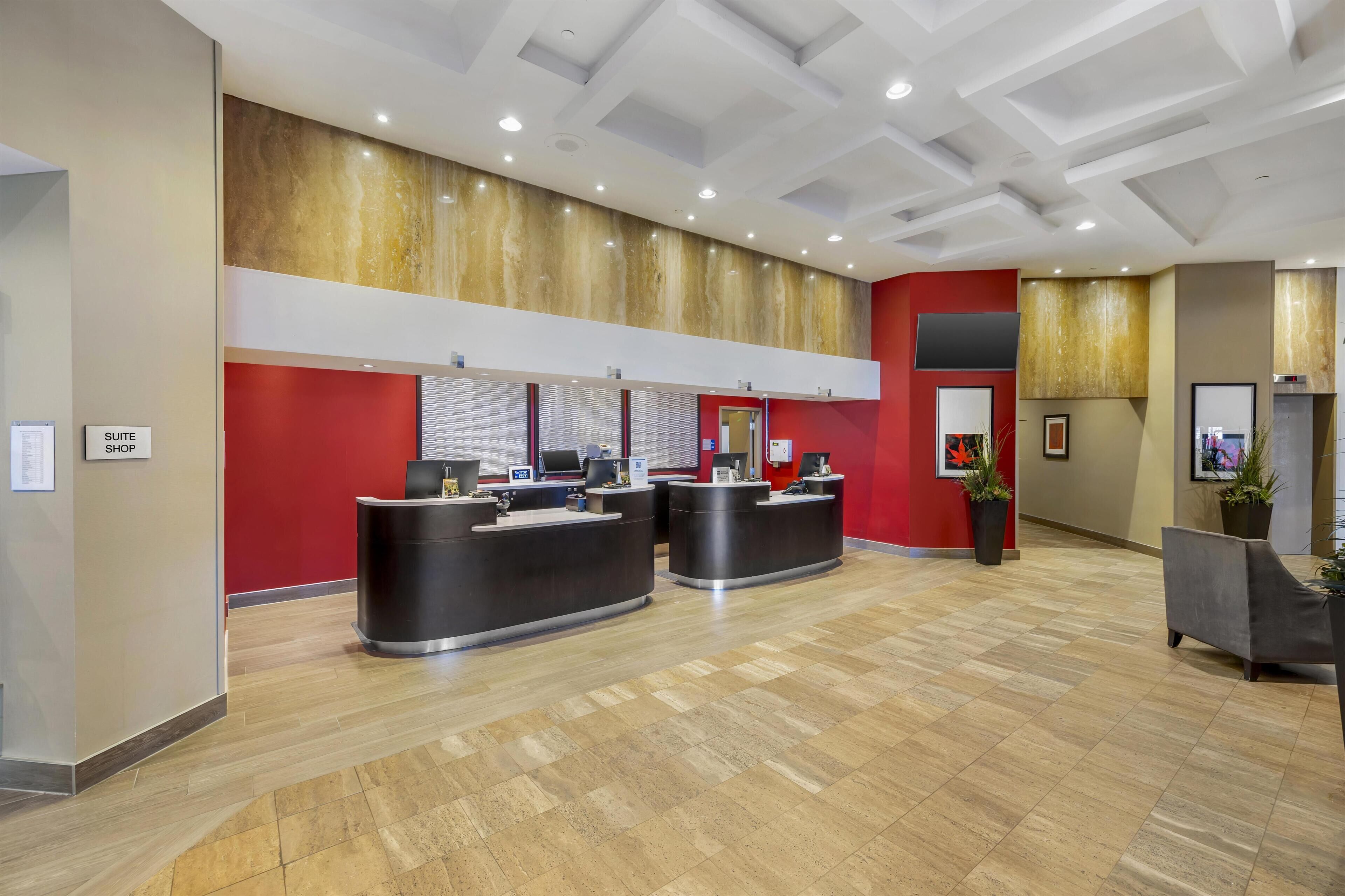 A hotel reception area with two black reception desks, a red accent wall, and a modern ceiling design.