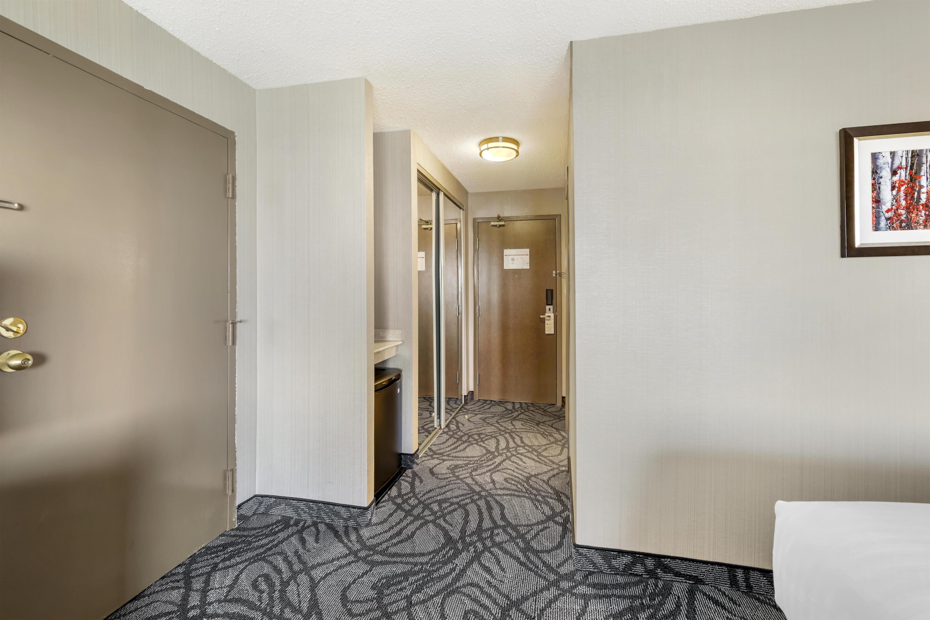 A hotel hallway with a patterned carpet, a framed picture on the wall, and a door with a handle.