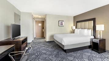 Een hotelkamer met een bed, nachtkastje, lamp, televisie, bureau en stoel.