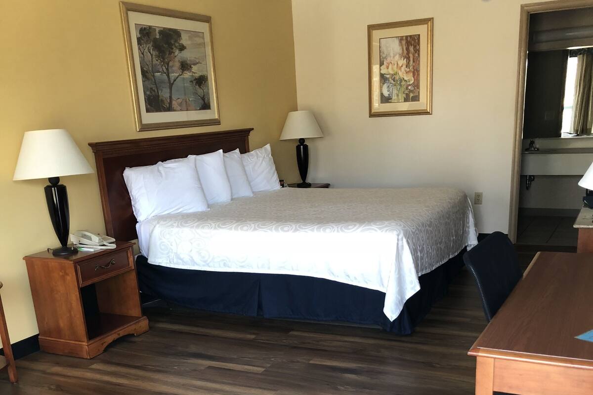 A hotel room with a large bed, two bedside tables with lamps, a wooden desk, and a chair.