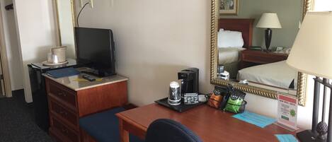 Una habitación de hotel con un escritorio de madera, televisión, cafetera y espejo.