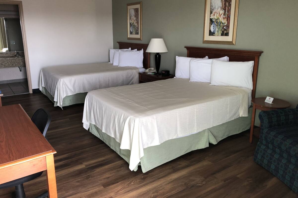 A hotel room with two single beds, a wooden desk, a chair, a small table, and two paintings on the walls.