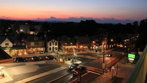A street view at dusk with buildings, cars, and a green signboard.