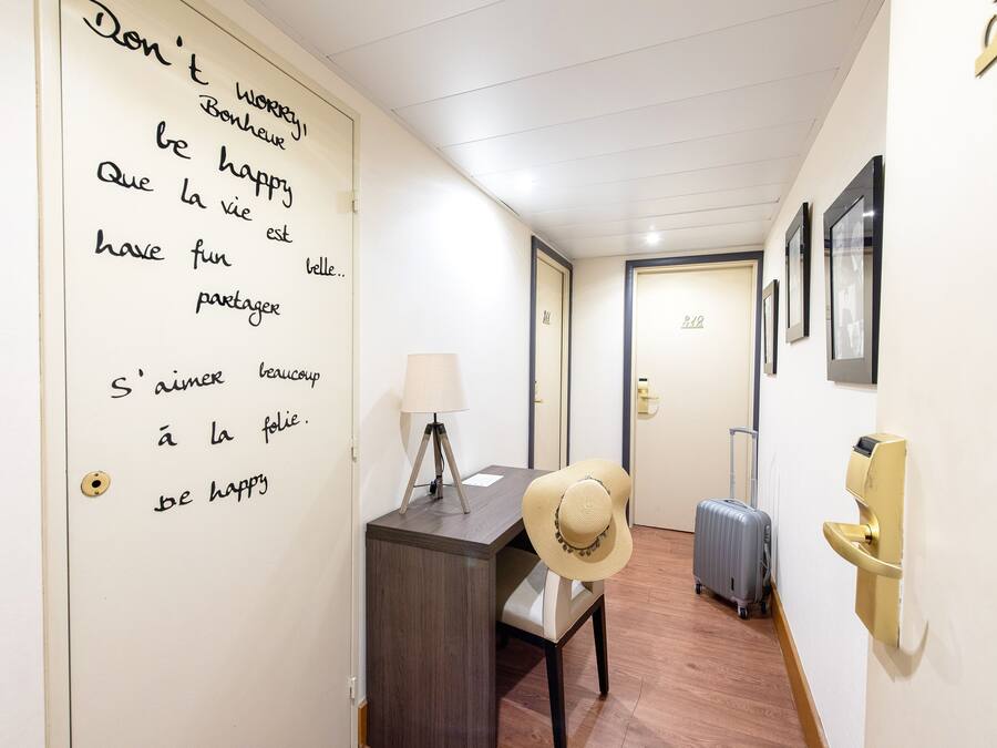 Un pasillo con un escritorio, una maleta y un sombrero. Se observa una pared con un mensaje escrito a mano en francés.