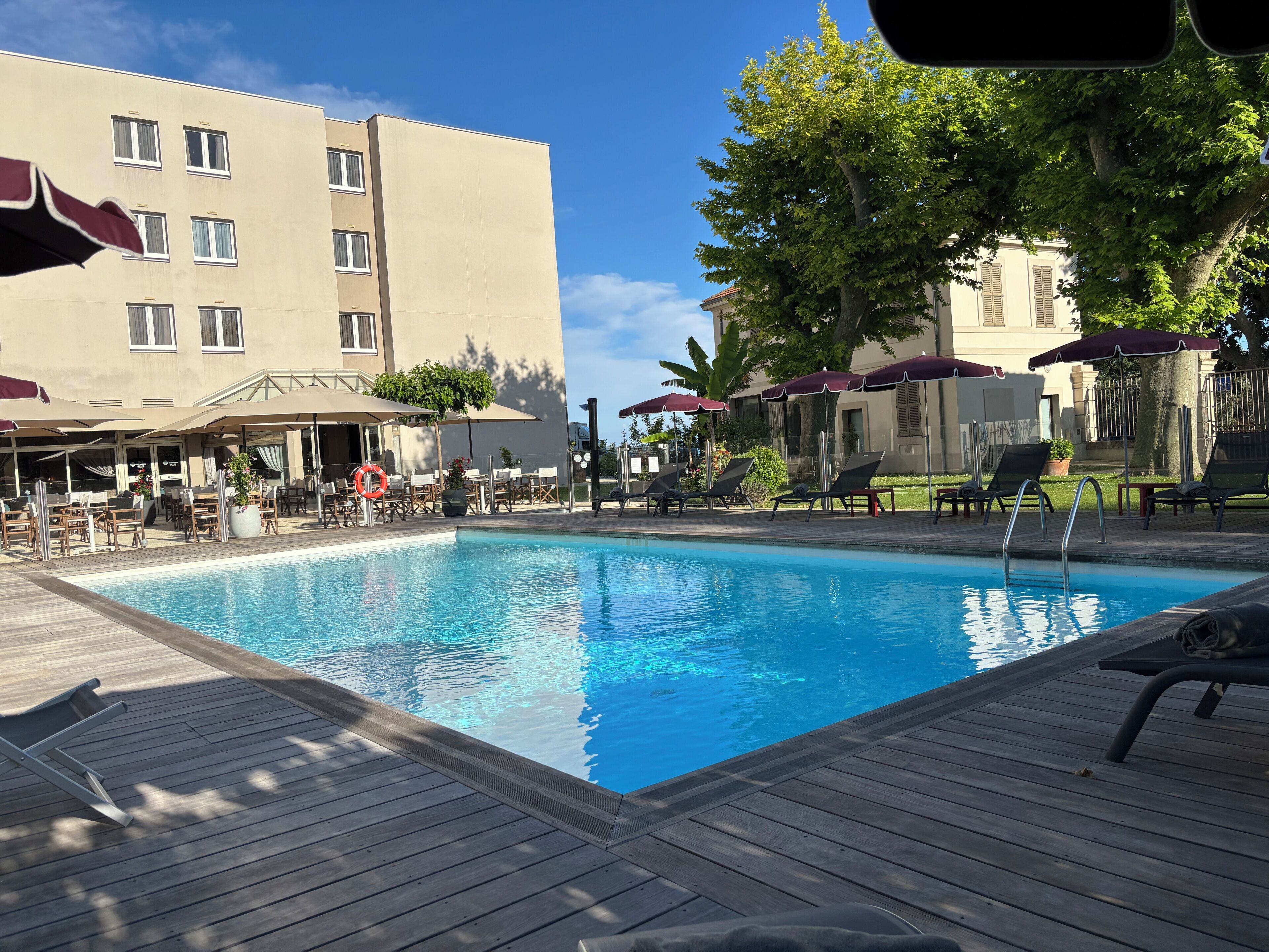 A swimming pool with lounge chairs and umbrellas, surrounded by buildings and trees.