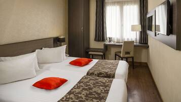 Habitación de hotel con dos camas, un escritorio, una silla y un televisor.