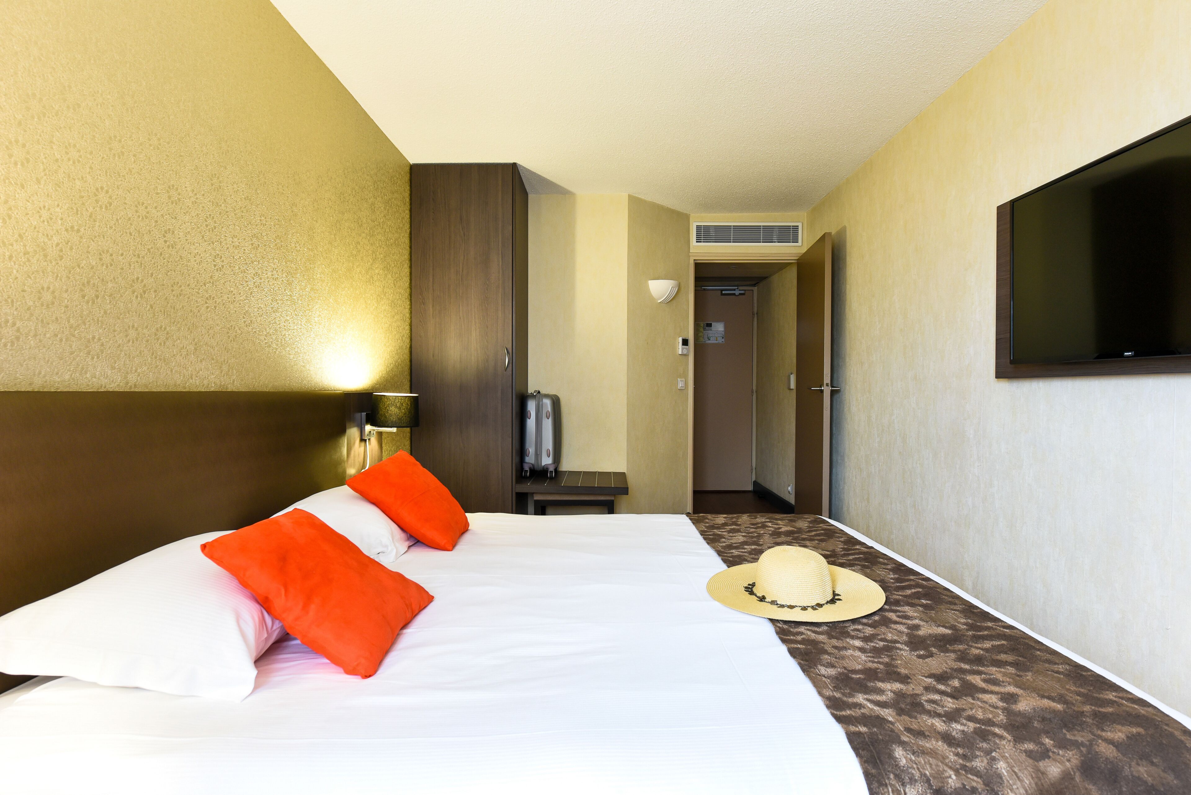 A hotel room with a bed, pillows, a television, and a hat on the floor.