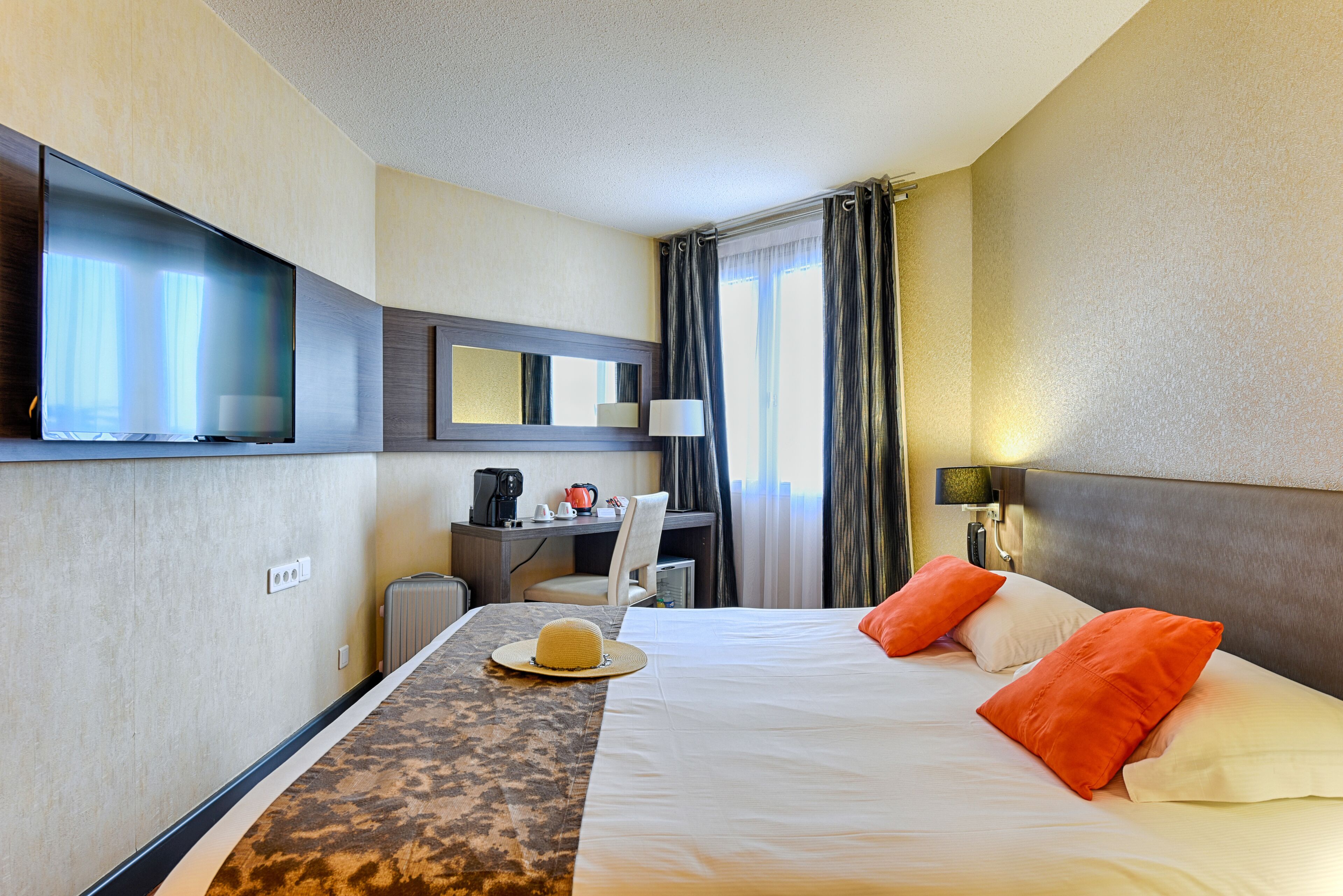 A hotel room with a bed, a desk, a television, and a window with curtains.