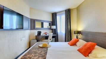 A hotel room with a bed, a desk, a television, and a window with curtains.